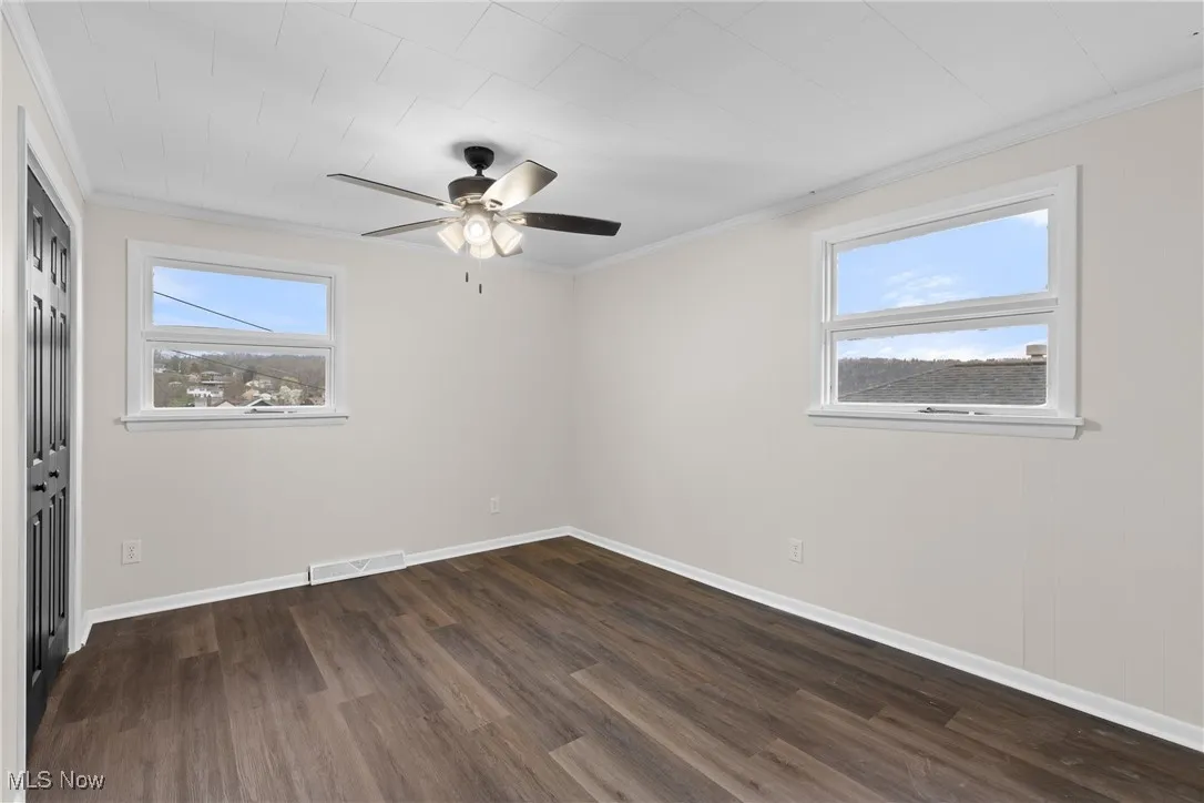 Unfurnished room featuring visible vents, crown molding, dark wood-type flooring, and a ceiling fan