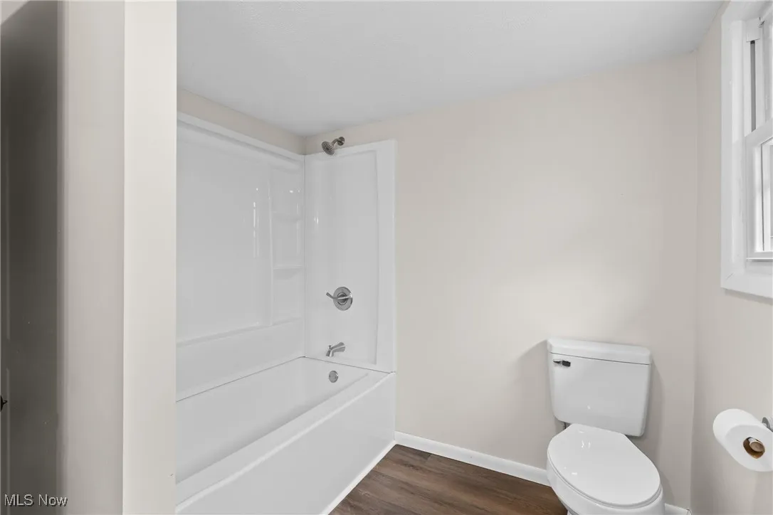 Bathroom with toilet, shower / tub combination, baseboards, and wood finished floors