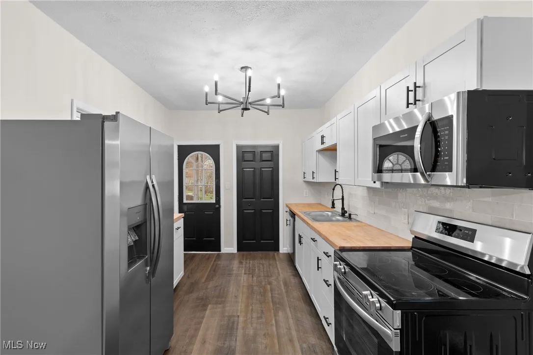Kitchen featuring a sink, a chandelier, tasteful backsplash, appliances with stainless steel finishes, and dark wood finished floors