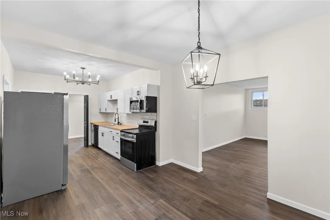 Kitchen featuring dark wood-style flooring, stainless steel appliances, white cabinetry, a sink, and an inviting chandelier