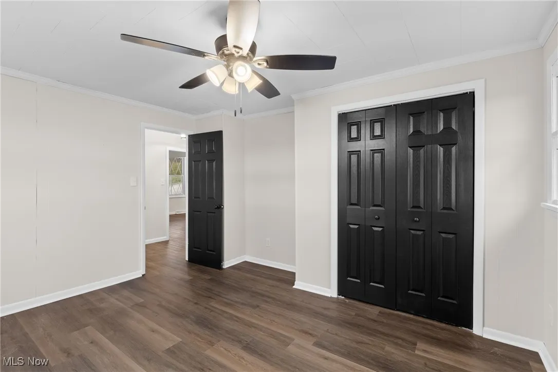 Unfurnished bedroom with ornamental molding, baseboards, dark wood finished floors, ceiling fan, and a closet