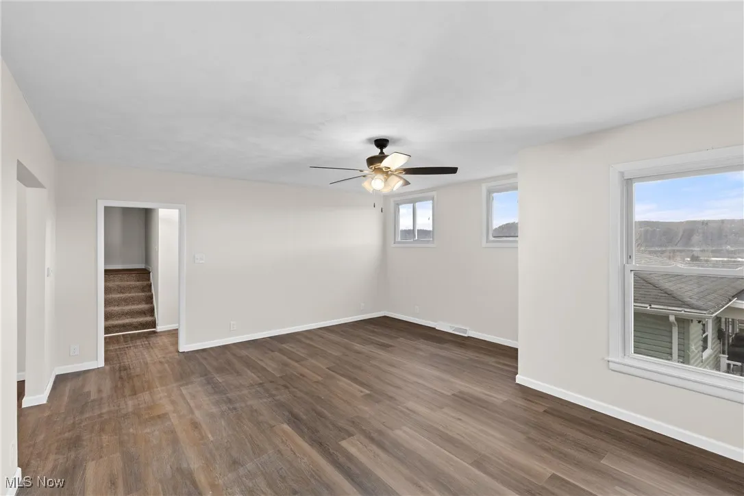 Spare room featuring baseboards, stairway, ceiling fan, and dark wood-type flooring