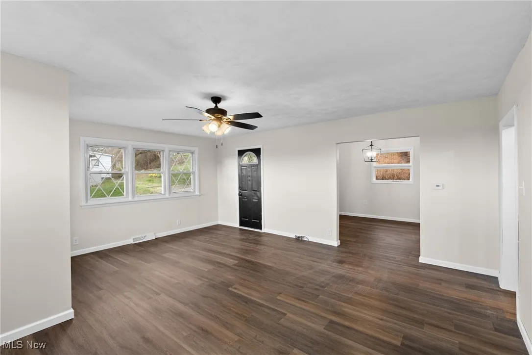 Unfurnished room featuring a ceiling fan, dark wood finished floors, baseboards, and visible vents
