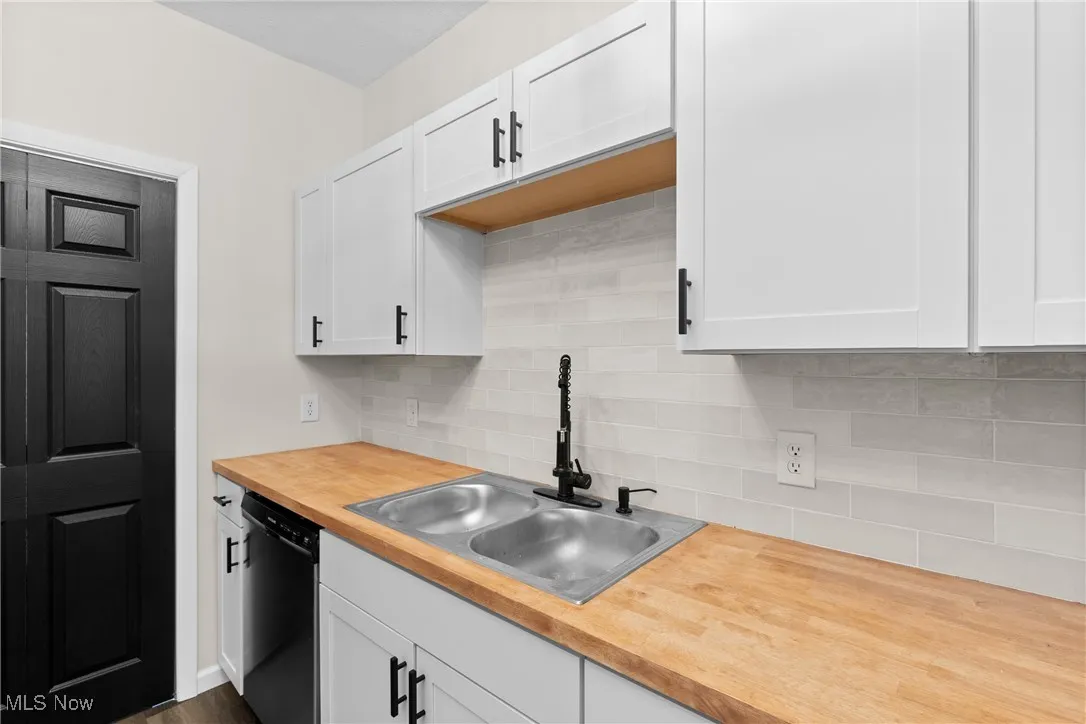 Kitchen featuring butcher block countertops, decorative backsplash, a sink, dishwasher, and white cabinets