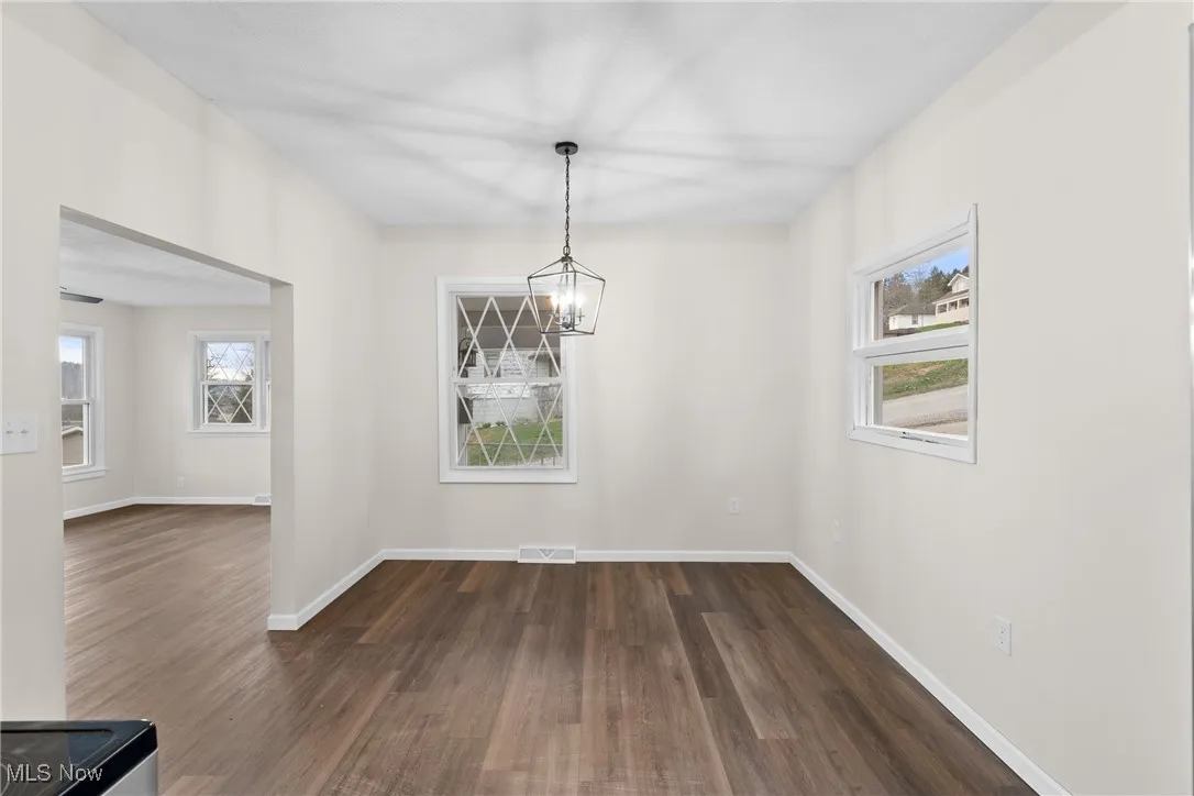 Unfurnished dining area with baseboards, visible vents, dark wood-type flooring, and an inviting chandelier