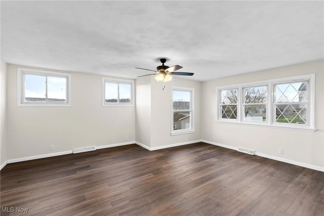 Empty room featuring dark wood-type flooring, baseboards, and visible vents