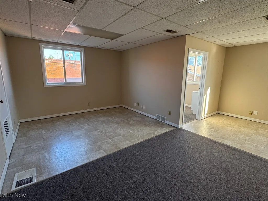 Carpeted spare room with baseboards, visible vents, and a drop ceiling