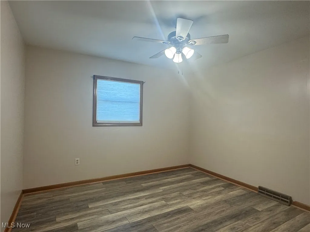Empty room with baseboards, dark wood-style flooring, visible vents, and a ceiling fan