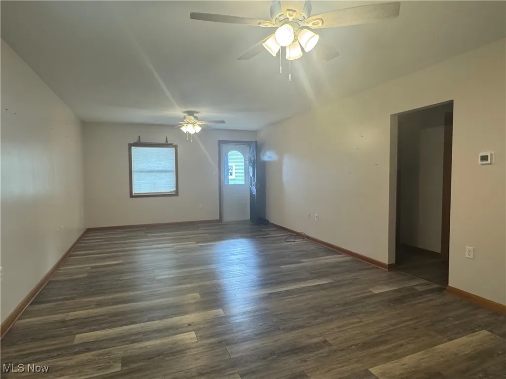 Spare room featuring baseboards, dark wood-style floors, and ceiling fan