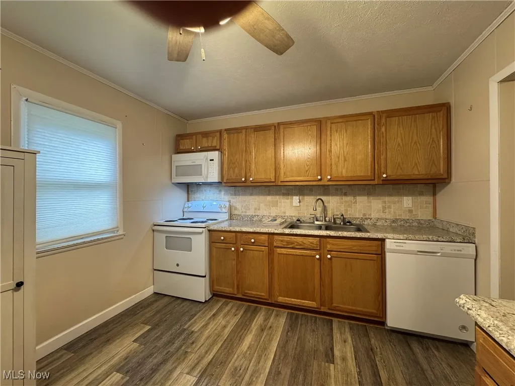 Kitchen with dark wood-style flooring, a sink, brown cabinetry, and white appliances