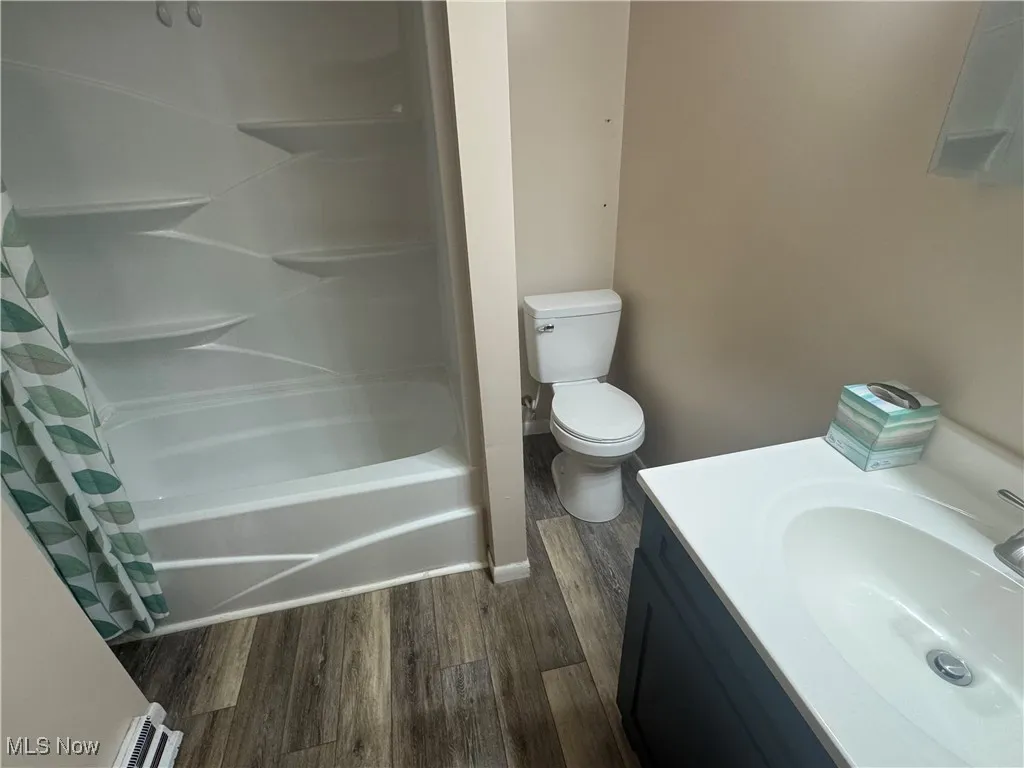 Bathroom with toilet, vanity, shower / bath combo, and wood finished floors