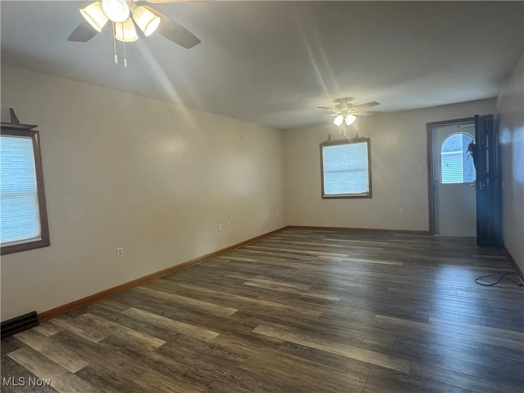 Empty room featuring dark wood-type flooring, baseboards, and ceiling fan