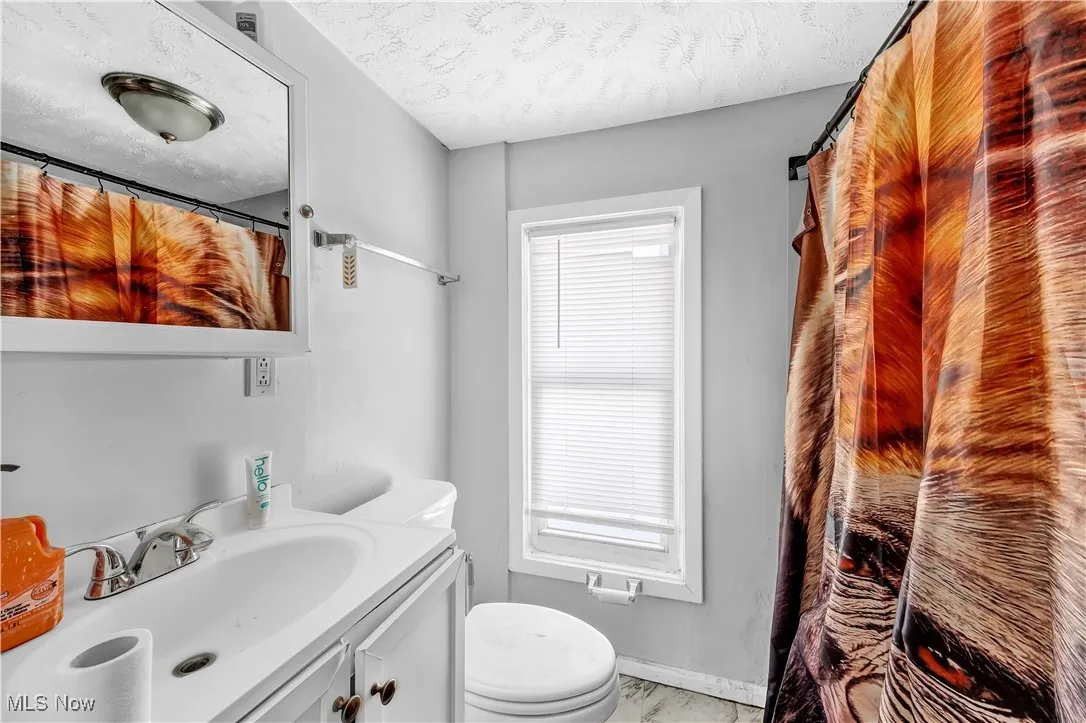 Full bath featuring baseboards, toilet, vanity, and a textured ceiling