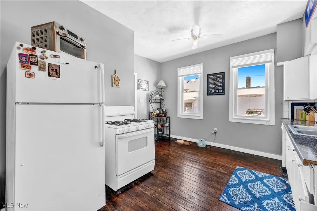 Kitchen featuring white appliances, baseboards, ceiling fan, white cabinetry, and dark wood-style floors