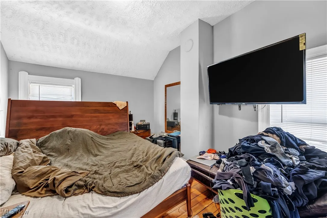 Bedroom with vaulted ceiling, wood finished floors, and a textured ceiling