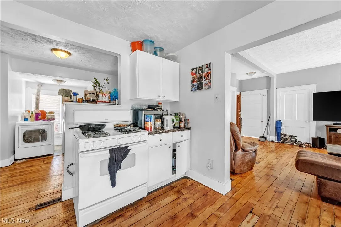 Kitchen with white cabinetry, washer / clothes dryer, white gas range oven, and light wood-type flooring