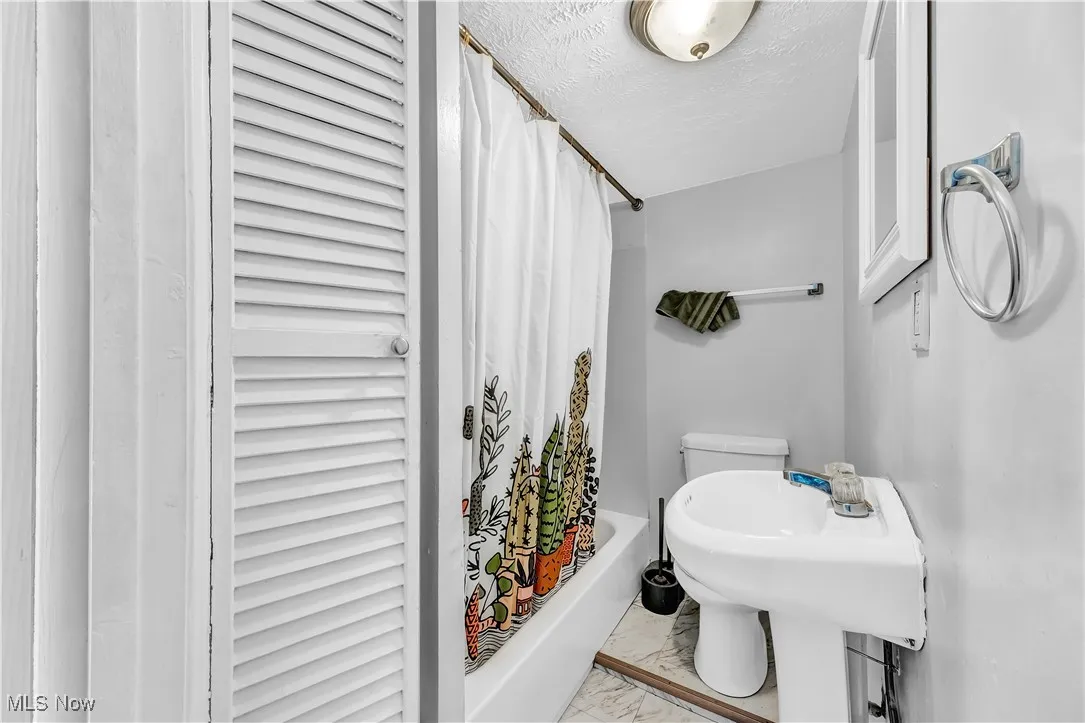 Bathroom featuring marble finish floor, shower / bathtub combination with curtain, toilet, and a textured ceiling