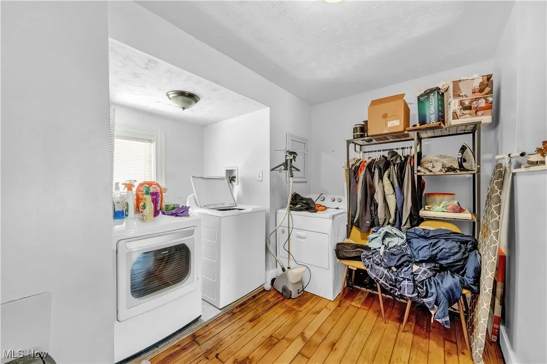 Clothes washing area featuring light wood-style flooring, washing machine and dryer, laundry area, and a textured ceiling