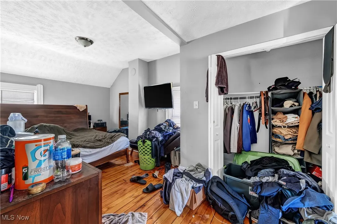 Bedroom with a textured ceiling, lofted ceiling, a closet, and hardwood / wood-style floors