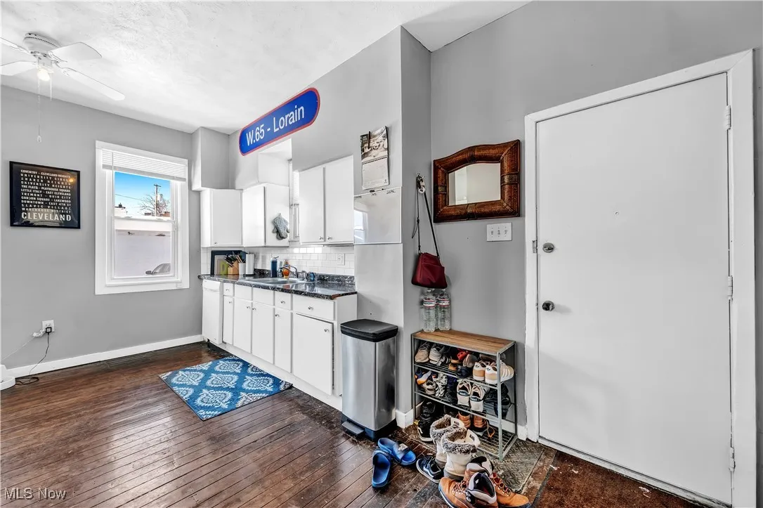 Kitchen featuring dark wood-type flooring, decorative backsplash, dark countertops, ceiling fan, and white cabinets