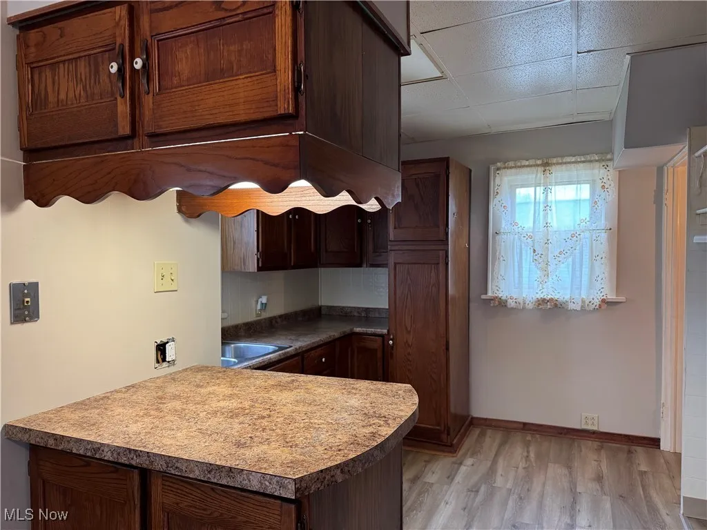 Kitchen featuring tasteful backsplash, baseboards, a drop ceiling, light wood-style flooring, and a peninsula