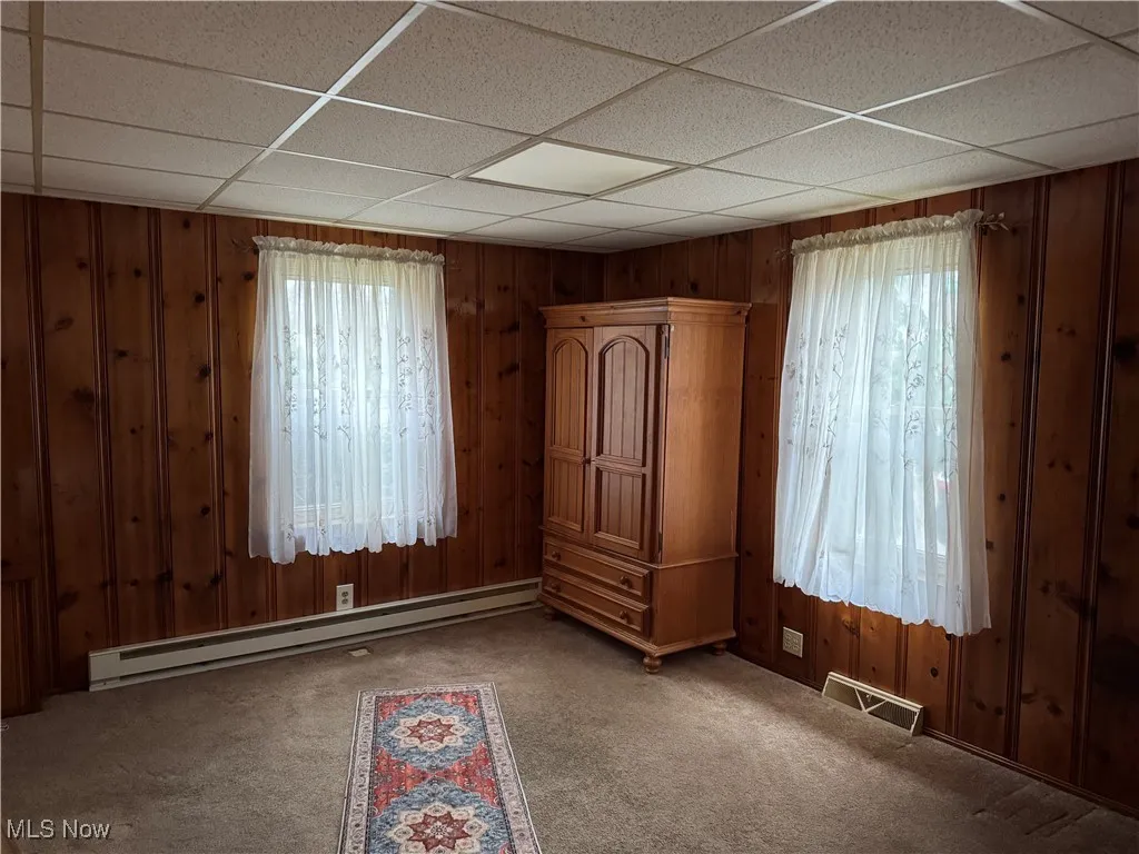 Carpeted spare room with baseboard heating, wooden walls, visible vents, and a paneled ceiling