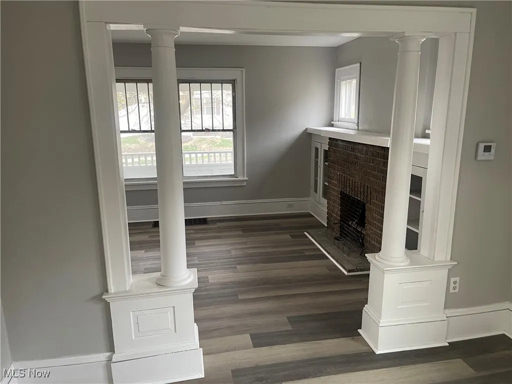 Unfurnished living room with a fireplace, ornate columns, dark wood-style flooring, and baseboards