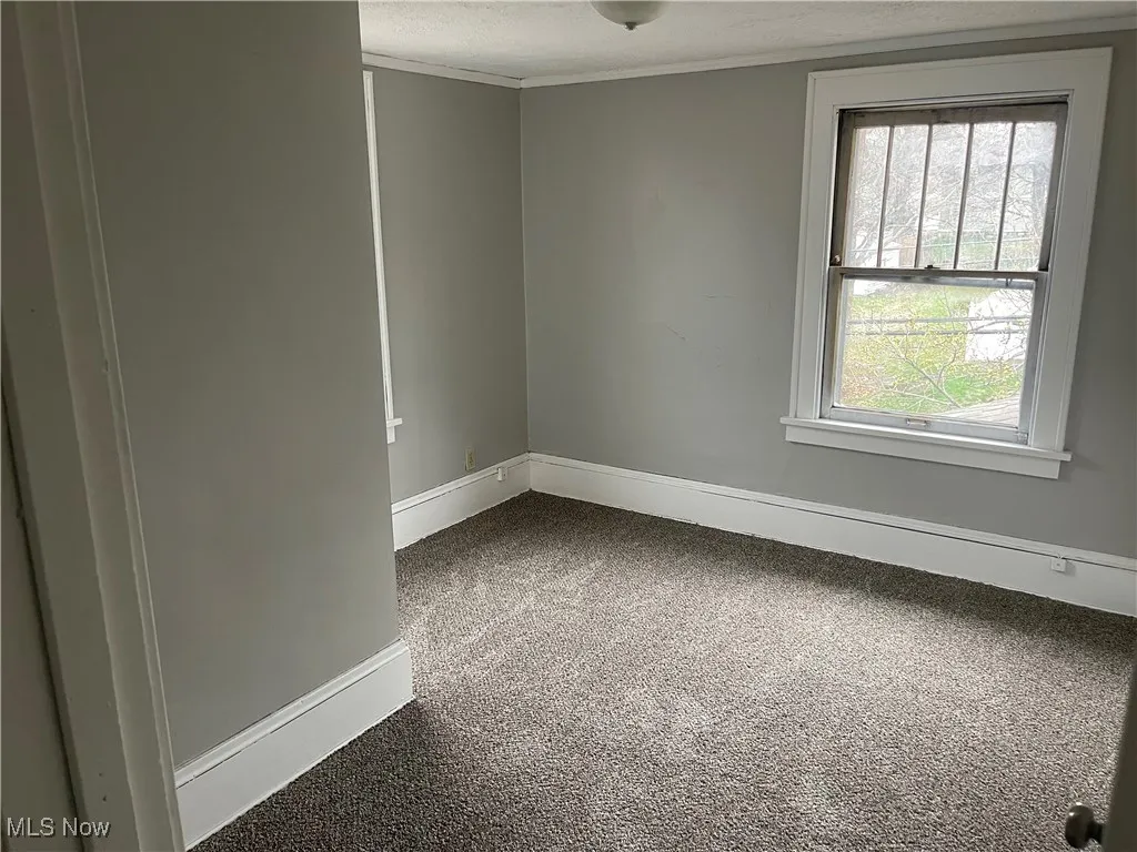 Empty room featuring dark carpet, crown molding, baseboards, and a textured ceiling