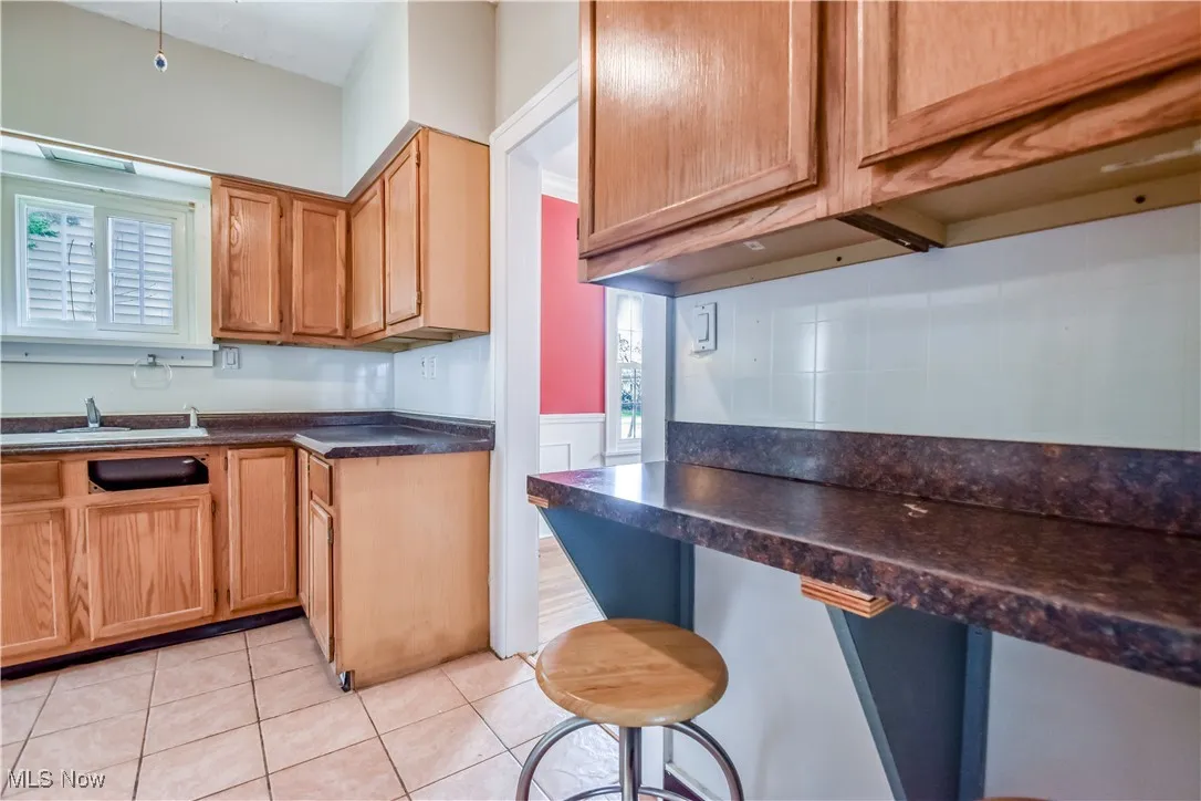 Kitchen featuring light tile patterned flooring, a breakfast bar, dark countertops, a sink, and wainscoting