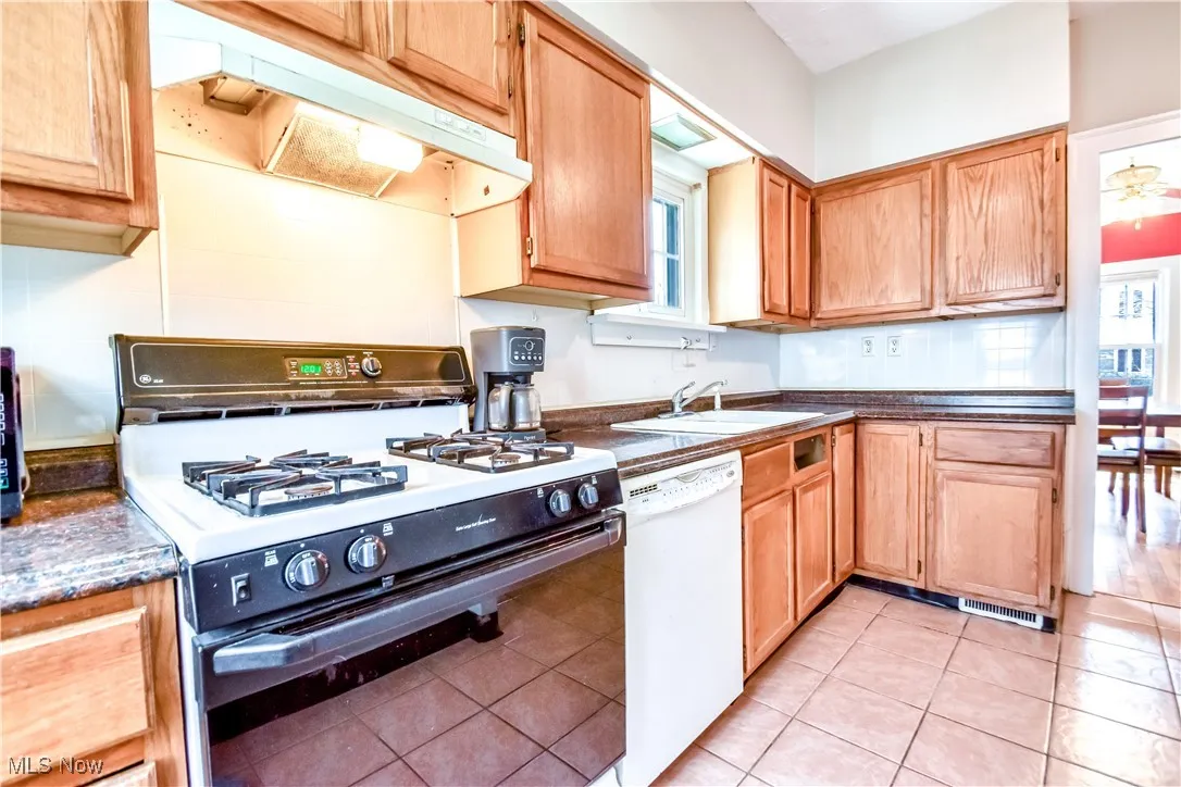 Kitchen featuring under cabinet range hood, a sink, dark countertops, and white appliances