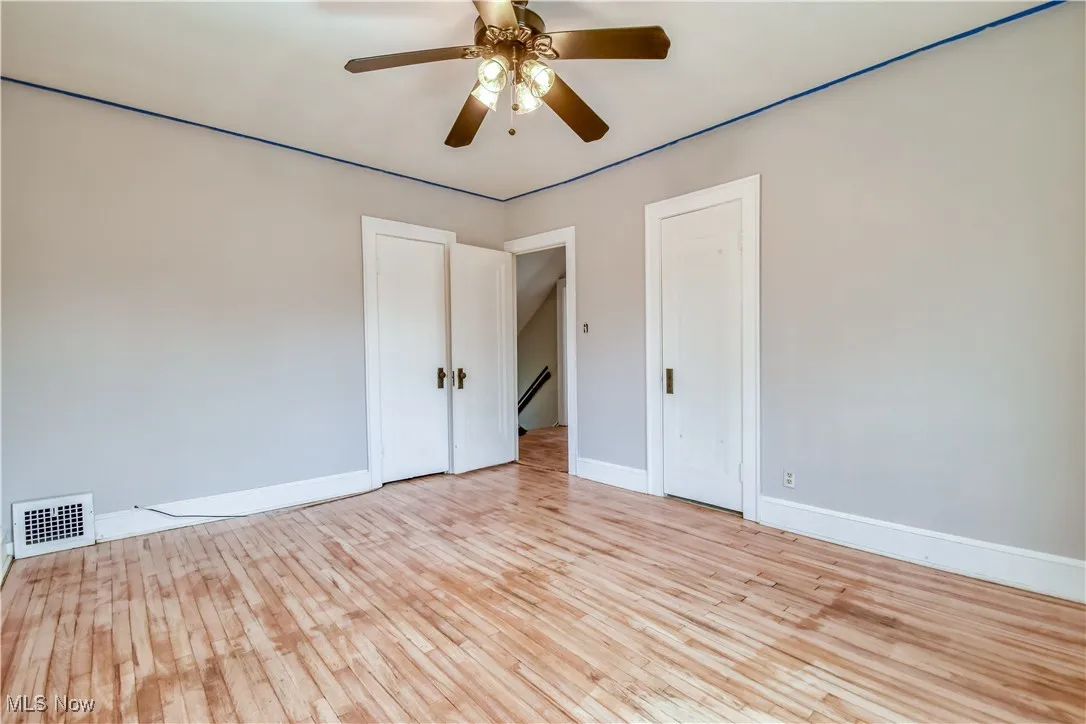Empty room with baseboards, a ceiling fan, visible vents, and light wood-type flooring