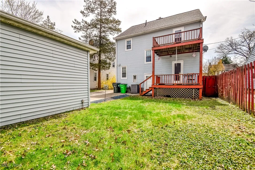 Rear view of house featuring a wooden deck, cooling unit, a fenced backyard, a balcony, and a lawn