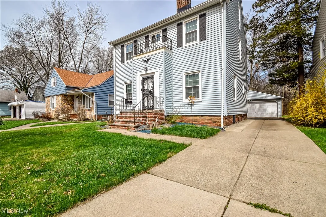 Colonial home featuring a chimney, an outdoor structure, a balcony, a front lawn, and a detached garage