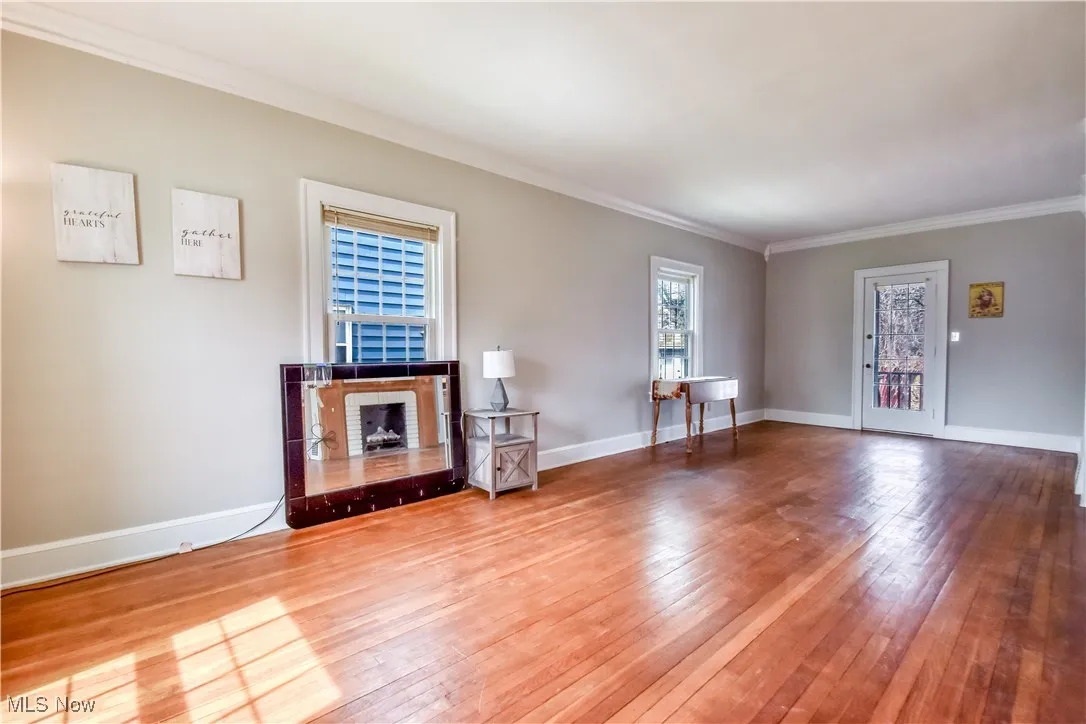Unfurnished living room featuring baseboards, ornamental molding, and wood-type flooring