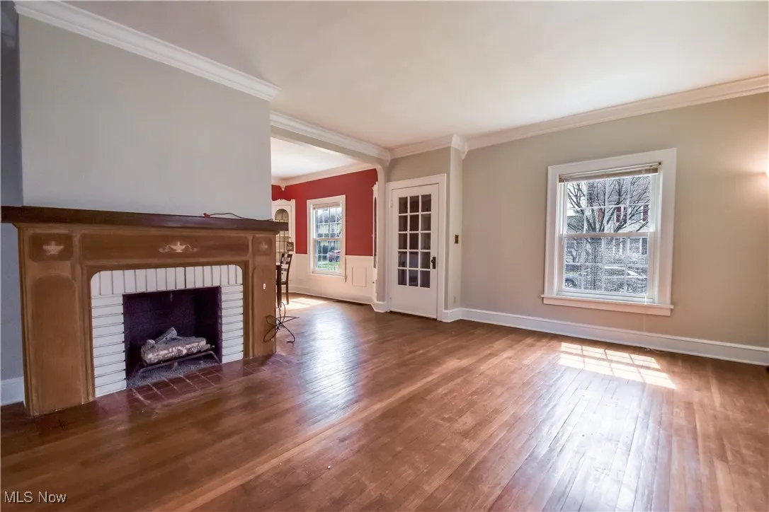 Unfurnished living room with baseboards, ornamental molding, a brick fireplace, and wood-type flooring