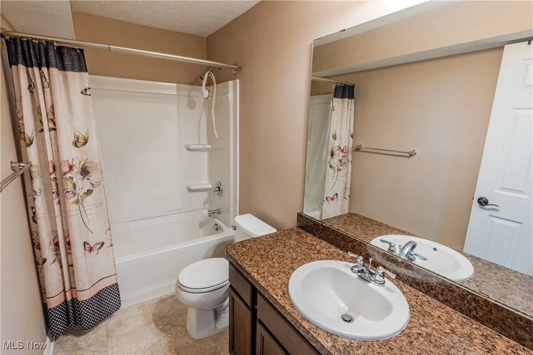 Full bathroom with shower / bath combination with curtain, toilet, vanity, and a textured ceiling