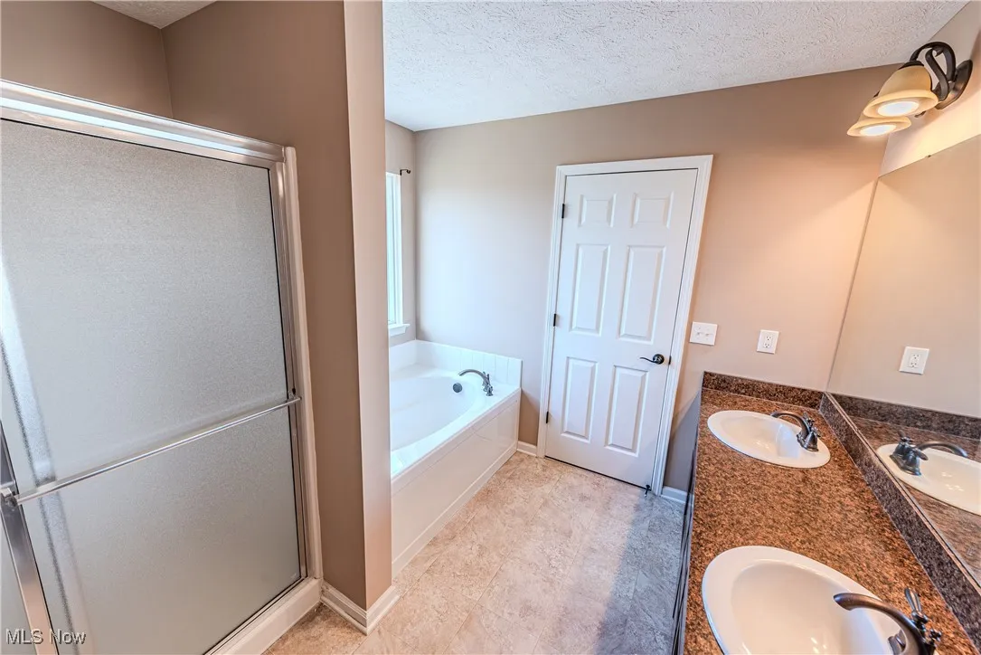 Primary en suite bathroom featuring a sink, a textured ceiling, a stall shower, and a bath