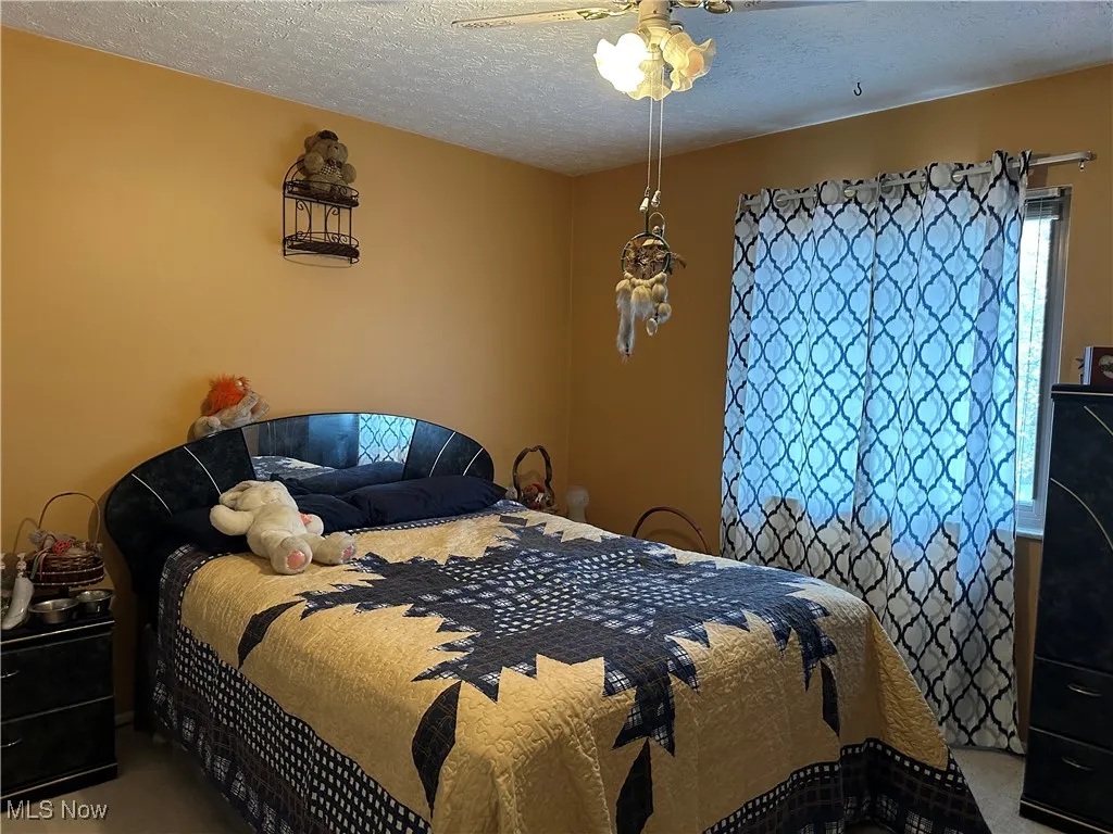 Carpeted bedroom with ceiling fan and a textured ceiling