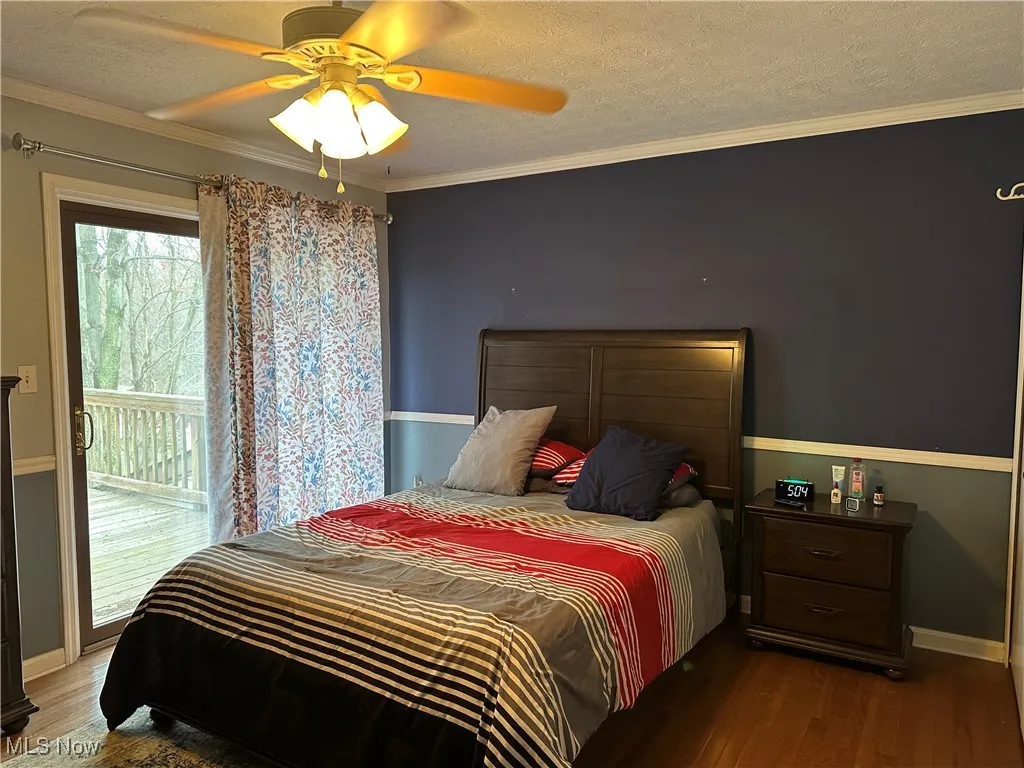Bedroom with access to exterior, wood finished floors, ornamental molding, and a textured ceiling