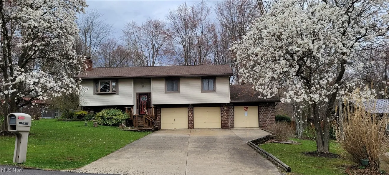 Raised ranch featuring concrete driveway, a chimney, brick siding, a front lawn, and a garage