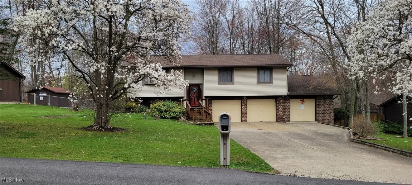 Raised ranch with driveway, an attached garage, brick siding, and a front yard