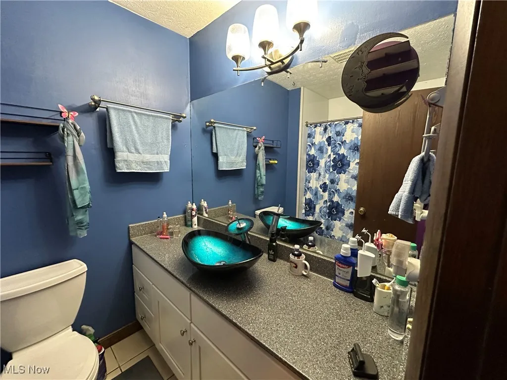 Bathroom with toilet, vanity, a textured ceiling, tile patterned flooring, and an inviting chandelier