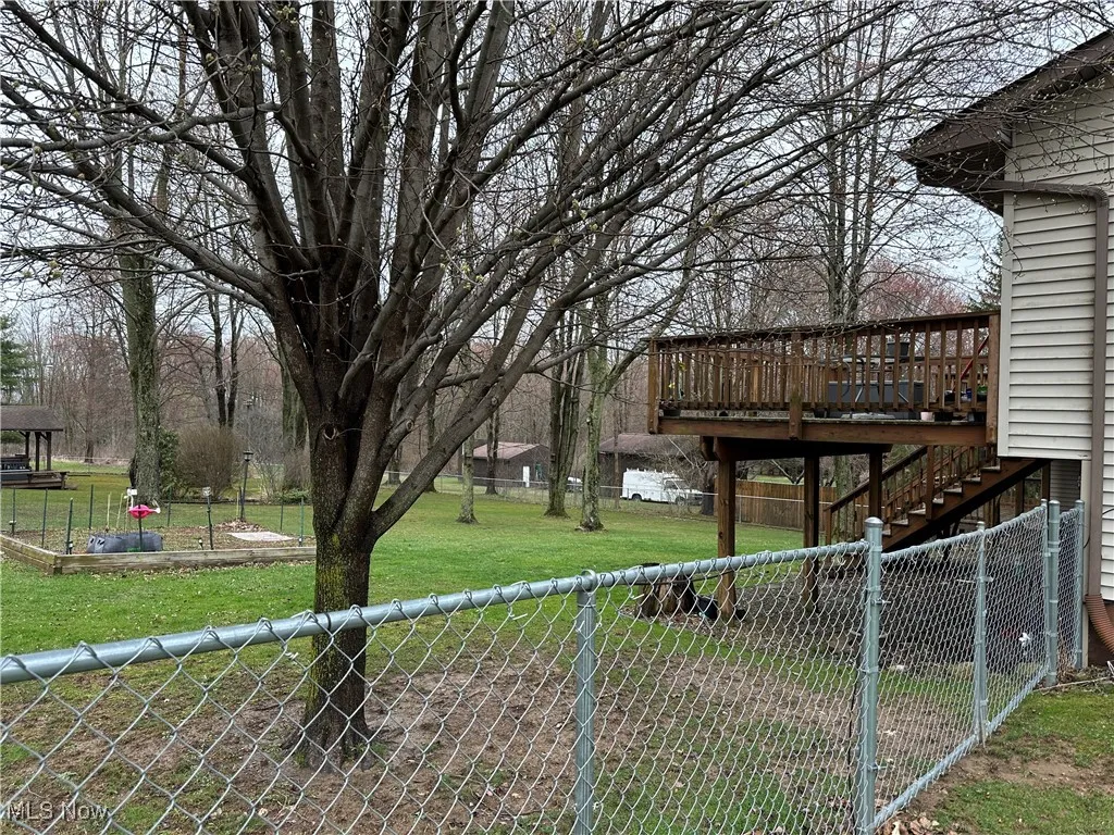 View of yard with fence, a wooden deck, and stairway