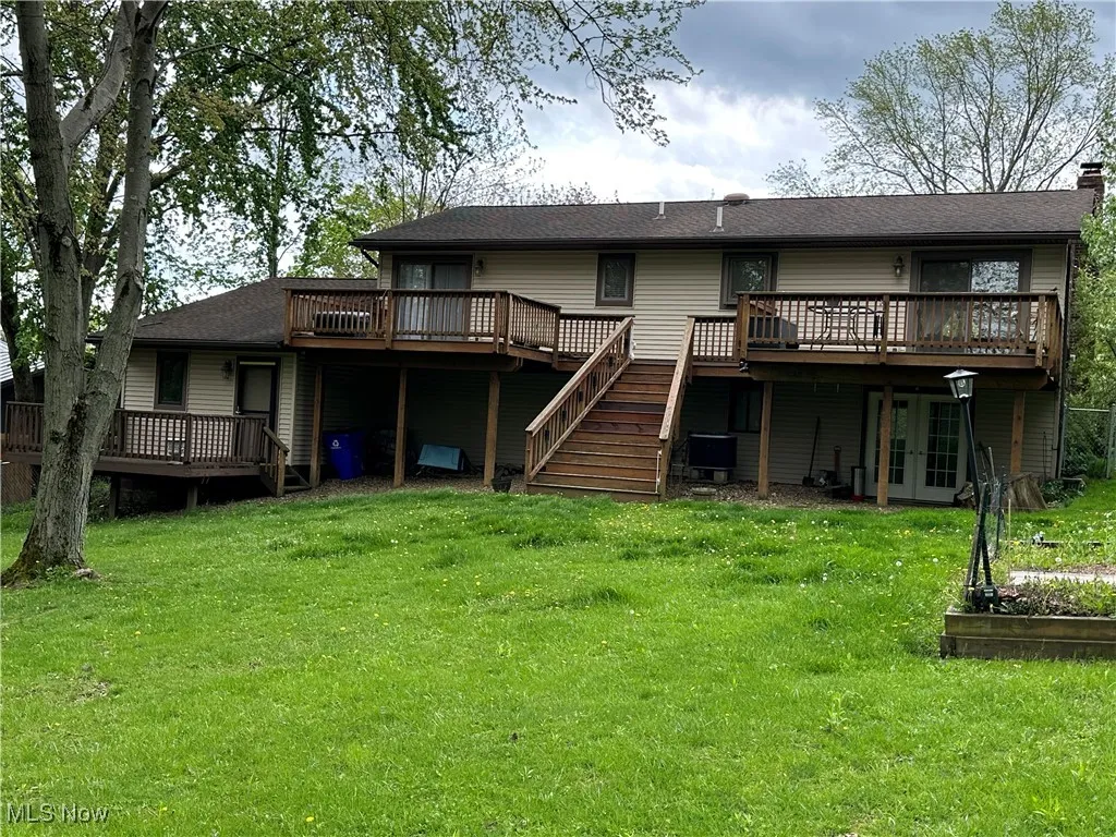 Back of property featuring french doors, a wooden deck, a vegetable garden, stairway, and a yard
