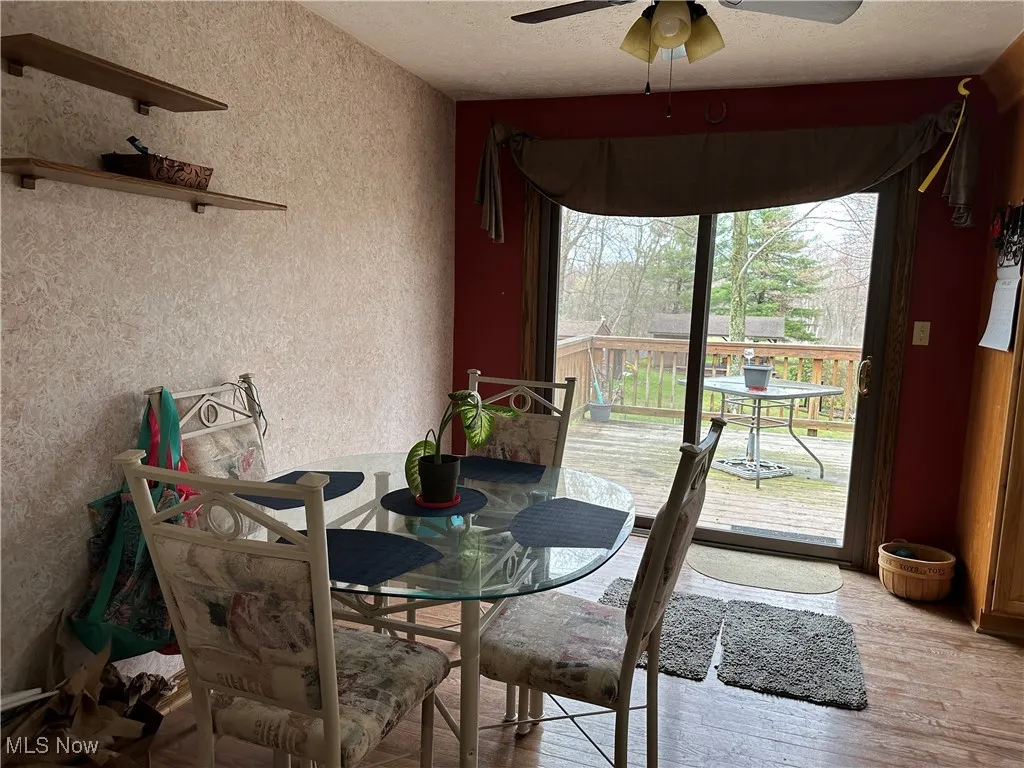 Dining area with a ceiling fan, a textured wall, light wood finished floors, and a textured ceiling