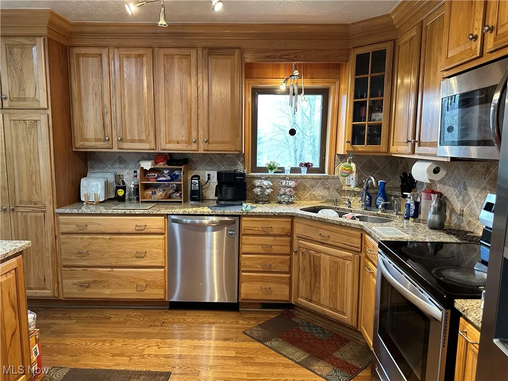 Kitchen featuring light stone counters, a sink, glass insert cabinets, light wood-style flooring, and stainless steel appliances