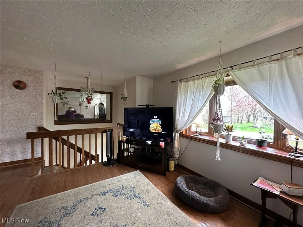 Sitting room featuring an upstairs landing, a textured ceiling, baseboards, and wood finished floors