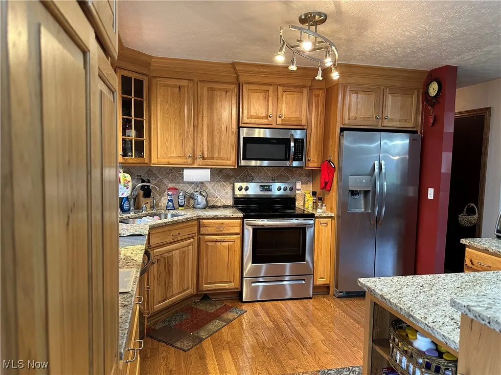 Kitchen with a sink, appliances with stainless steel finishes, brown cabinets, and light wood-type flooring
