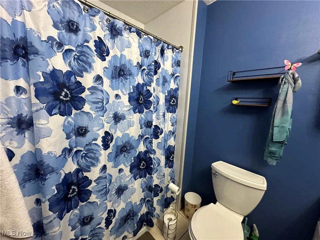 Bathroom featuring toilet, a shower with shower curtain, and a textured ceiling