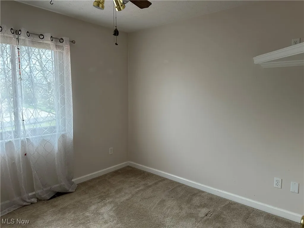 Carpeted spare room featuring baseboards and ceiling fan